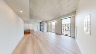 This thoughtfully designed urban residence offers a compelling blend of industrial and contemporary aesthetics across a single floor. The open-concept living and kitchen area is the heart of the space, showcasing a dramatic exposed concrete ceiling, light-washed hardwood flooring, and floor-to-ceiling black-framed windows that flood the interior with natural light and frame sweeping city views. The kitchen features warm wood cabinetry paired with white quartz countertops, stainless steel appliances, and a clean, minimalist layout that flows seamlessly into the generous living area. Exposed concrete columns add architectural character throughout, providing a striking contrast to the bright white walls. The bedroom is a serene retreat, benefiting from its own large window with urban views and the same refined hardwood flooring. Two bathrooms serve the residence: one features a glass-enclosed stand-up shower, while the second offers a full soaking tub and shower combination with stone-tile flooring and a sleek white vanity. A hallway connects the private spaces efficiently. The overall ambiance is modern and airy, with an industrial-chic character defined by raw concrete, natural wood tones, and an abundance of natural light.
