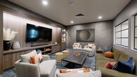 This theater space is designed as a sophisticated media lounge, combining comfortable viewing with contemporary interior design. The focal point of the room is a large flat-screen television mounted within a built-in wood-paneled entertainment wall, flanked by open shelving displaying decorative objects and media accessories. A soundbar and media console with open storage compartments complete the entertainment setup, providing both functionality and visual appeal.

The seating arrangement is thoughtfully curated, featuring a mix of plush light gray accent chairs, an olive-toned sofa, and a tufted dark leather ottoman that doubles as a central coffee table. Two cylindrical upholstered stools provide flexible additional seating. Colorful accent pillows in warm orange, rust, and blue tones add vibrancy against the neutral furnishings.

The room's walls are finished in a textured concrete-style treatment in a deep gray tone, lending an urban, contemporary ambiance. Large framed artwork, including an abstract circular piece and vibrant multi-panel prints, adds artistic character. Interior windows with black steel frames allow views into adjacent spaces, while recessed lighting provides a warm, even illumination. The patterned blue and gray area rug anchors the seating arrangement and reinforces the space's modern aesthetic.