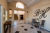 This expansive single-floor community space makes a striking first impression with a soaring two-story grand lobby, featuring elegant tilework with an octagonal inlay, a decorative chandelier, arched architectural details, and abundant natural light streaming through clerestory windows. A carpeted staircase with brass stanchions leads to an upper mezzanine level, adding visual depth to the dramatic entrance.

The dining area is bright and inviting, wrapped in large multi-pane windows that frame lush outdoor greenery. Warm hardwood flooring and a pendant chandelier complement the classic furnishings, creating an ideal gathering space.

A dedicated racquetball court offers a full regulation playing surface with polished hardwood floors, crisp white walls, and overhead skylights — ready for active recreation. Adjacent amenities include an indoor spa and pool area, with tile-accented walls and large windows overlooking an outdoor pool, providing a relaxing retreat year-round.

The business center is equipped with dual computer workstations, a printer, and comfortable seating beneath a skylight. A clean, functional kitchen features white cabinetry, stone-toned countertops, and wood flooring. The home theater room rounds out the amenities with plush leather recliner seating, recessed lighting, and a large-screen display for an immersive viewing experience.