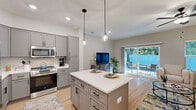 Located at 5180 NE 71st Ave in Wildwood, Florida, this well-designed two-story home offers 3 bedrooms and 4 bathrooms spread evenly across two floors. The main level features an open-concept layout combining the living room, dining area, and kitchen into one cohesive, light-filled space. The kitchen is outfitted with gray shaker-style cabinetry, white quartz countertops, stainless steel appliances, and a central island with pendant lighting — ideal for both cooking and casual dining. The living room is bright and airy, featuring light hardwood-style flooring, a ceiling fan, and large sliding glass doors that open to an outdoor patio with views of mature trees, seamlessly blending indoor and outdoor living. A hallway and staircase connect the main floor to the upper level, which hosts the bedrooms and additional bathrooms. Each bedroom features ceiling fans, light flooring, and access to well-finished bathrooms with gray vanities and white quartz countertops. The primary bedroom includes a private en-suite bath. Additional spaces include a laundry room, utility room, and multiple closets throughout. The home's clean, neutral palette and modern finishes create a cohesive and comfortable atmosphere throughout.