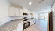 Located at 1418 Frontier Valley Dr in Austin, TX, this efficiently designed single-floor unit offers a clean, modern aesthetic throughout. Light wood-tone flooring flows continuously across the entire space, providing a cohesive and airy feel. The open-concept kitchen and living area serves as the heart of the unit, where the kitchen features white shaker-style cabinetry, granite countertops with a subtle speckled pattern, white subway tile backsplash, and a full suite of stainless steel appliances including a range, microwave, refrigerator, and dishwasher. The living area is bright and welcoming, benefiting from a sliding glass door that opens to a private balcony with outdoor views, complemented by an additional window fitted with white plantation shutters. A ceiling fan with a brushed gold finish adds both function and style to the space. The bathroom continues the consistent design language with light blue-gray walls, white subway tile surrounding the tub-shower combo, a granite-topped white vanity, and wood-tone flooring. A dedicated closet provides practical storage. The unit's neutral white walls and abundant natural light create a fresh, move-in-ready environment well-suited for comfortable everyday living.