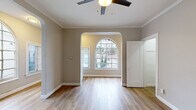 Located at 1733 N Cherokee Ave in the heart of Hollywood, Los Angeles, this single-story unit showcases a thoughtful blend of classic architectural charm and modern finishes. The living area immediately impresses with its elegant arched doorways and large arched windows that flood the space with natural light, offering views of the surrounding neighborhood. Warm-toned, hardwood-style flooring runs throughout the main living areas, complementing the neutral gray and taupe wall palette and crisp white crown molding that lines the ceilings. Ceiling fans in the living and bedroom areas provide both comfort and a timeless aesthetic touch. The layout flows naturally from the front living area through the arched passage into an adjoining room, creating a connected yet defined sense of space. The bedroom is generously sized, featuring a dedicated closet and direct access to the bathroom. The bathroom is finished in clean white tile, complete with a full soaking tub and shower combination, a toilet, and a window for natural ventilation. The kitchen area is positioned toward the rear of the unit, with white cabinetry visible from the open layout. Throughout the space, white panel doors and classic baseboards reinforce the cohesive, well-maintained character of this Hollywood residence.
