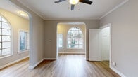 Located at 1733 N Cherokee Ave in the heart of Hollywood, Los Angeles, this single-story unit showcases a thoughtful blend of classic architectural charm and modern finishes. The living area immediately impresses with its elegant arched doorways and large arched windows that flood the space with natural light, offering views of the surrounding neighborhood. Warm-toned, hardwood-style flooring runs throughout the main living areas, complementing the neutral gray and taupe wall palette and crisp white crown molding that lines the ceilings. Ceiling fans in the living and bedroom areas provide both comfort and a timeless aesthetic touch. The layout flows naturally from the front living area through the arched passage into an adjoining room, creating a connected yet defined sense of space. The bedroom is generously sized, featuring a dedicated closet and direct access to the bathroom. The bathroom is finished in clean white tile, complete with a full soaking tub and shower combination, a toilet, and a window for natural ventilation. The kitchen area is positioned toward the rear of the unit, with white cabinetry visible from the open layout. Throughout the space, white panel doors and classic baseboards reinforce the cohesive, well-maintained character of this Hollywood residence.