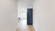 This well-appointed one-bedroom, one-bathroom residence at 501 Orleans St in Richmond, Virginia offers a thoughtfully designed modern interior across a single floor. Light-toned hardwood flooring flows throughout the main living areas, complementing the clean white walls and creating a bright, cohesive aesthetic.

The open-concept kitchen and living area serves as the heart of the home. The kitchen is a standout feature, showcasing bold navy-blue cabinetry, a white quartz waterfall island with an undermount sink, stainless steel appliances including a French door refrigerator and range, and a sleek pendant light fixture. A window above the kitchen provides natural light and outdoor views.

The bedroom offers a comfortable and quiet retreat, finished with plush carpet flooring and a custom wood built-in wardrobe that provides generous storage. Large windows frame picturesque views of the surrounding Richmond neighborhood and rolling landscape, filling the room with natural light.

The bathroom is clean and modern, featuring large-format tile flooring, a dark vanity with gold hardware accents, and a full tub-shower combination enclosed by sliding glass doors with brushed nickel finishes.

Throughout the space, a consistent design language of crisp whites, natural wood tones, and bold navy accents creates a polished and contemporary living environment.