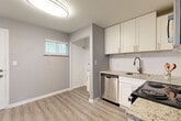 This single-floor unit offers a practical and modern layout across two bedrooms and two bathrooms. Light gray walls and light-toned luxury vinyl plank flooring run consistently throughout, creating a cohesive, contemporary aesthetic. White trim and baseboards provide clean contrast against the neutral palette.

The kitchen is well-appointed with white shaker-style cabinetry, granite-look countertops, a white subway tile backsplash, and stainless steel appliances including an electric range, built-in microwave, dishwasher, and undermount sink. The adjacent living and dining area receives natural light through a window with blinds and features a separate entry door.

Both bedrooms include windows overlooking outdoor greenery and are equipped with ceiling fans. The primary bedroom offers a comfortable, functional footprint, while the second bedroom mirrors the same clean design and flooring.

The two bathrooms are notably finished with full-surround wood-look porcelain tile in the tub/shower enclosures, brushed nickel fixtures, and a windowed wall for natural light. A central hallway connects the rooms efficiently, contributing to the unit's organized and functional flow.