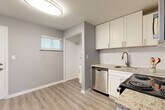 This single-floor unit offers a practical and modern layout across two bedrooms and two bathrooms. Light gray walls and light-toned luxury vinyl plank flooring run consistently throughout, creating a cohesive, contemporary aesthetic. White trim and baseboards provide clean contrast against the neutral palette.

The kitchen is well-appointed with white shaker-style cabinetry, granite-look countertops, a white subway tile backsplash, and stainless steel appliances including an electric range, built-in microwave, dishwasher, and undermount sink. The adjacent living and dining area receives natural light through a window with blinds and features a separate entry door.

Both bedrooms include windows overlooking outdoor greenery and are equipped with ceiling fans. The primary bedroom offers a comfortable, functional footprint, while the second bedroom mirrors the same clean design and flooring.

The two bathrooms are notably finished with full-surround wood-look porcelain tile in the tub/shower enclosures, brushed nickel fixtures, and a windowed wall for natural light. A central hallway connects the rooms efficiently, contributing to the unit's organized and functional flow.