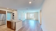 North Grove B2A is a thoughtfully designed 860-square-foot, single-story apartment located in Riverside, CA 92501. This 2-bedroom, 2-bathroom residence features a modern aesthetic with clean lines and neutral tones throughout. The open-concept kitchen and living area serves as the heart of the home, showcasing a stylish kitchen equipped with two-tone cabinetry—white upper cabinets paired with warm wood-finish lowers—quartz countertops, a subway tile backsplash, stainless steel appliances including a gas range, microwave, and refrigerator, and a central island with a sink. The living area features light hardwood-style flooring and multiple windows that invite an abundance of natural light. The primary bedroom spans 140 square feet with plush carpeting and a dedicated walk-in closet with wire shelving. The second bedroom also features carpet flooring and a bright window with exterior views of the community. Both bathrooms are finished with wood-style flooring and full tub/shower combinations. Additional conveniences include an in-unit laundry area and covered parking visible from the unit. The community exterior reflects a contemporary multi-story architectural design with balconies and structured parking.
