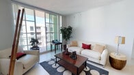 This single-floor residence is designed with a clean, contemporary aesthetic characterized by crisp white walls, large-format light tile flooring throughout the main living areas, and an open-concept layout that promotes a sense of spaciousness and easy flow between rooms.

The living area is generously sized, anchored by floor-to-ceiling windows that invite abundant natural light and views of the surrounding cityscape. The space transitions seamlessly into the dining area, which accommodates a full dining set alongside a freestanding shelving unit, ideal for storage or display.

The kitchen features warm wood cabinetry, sleek black granite countertops, a breakfast bar peninsula that opens to the living and dining spaces, and stainless steel appliances. This open configuration makes the kitchen both functional and socially connected to the rest of the home.

Two bathrooms are finished with beige marble-toned tile, dark wood vanities, and stone-topped counters. The primary bathroom includes a soaking tub and a double-sink vanity with a large mirror, while the second bathroom offers a single vanity and tub.

A carpeted bedroom provides a quieter, softer retreat with a window that draws in natural light. The overall ambiance of the space is modern, airy, and refined.