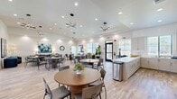 Located at 1650 Huntington Dr in Roseville, CA, this single-story community clubhouse offers a generously proportioned layout designed for gathering, socializing, and everyday convenience. The centerpiece is a bright, open great room featuring vaulted ceilings, light hardwood-style flooring, and an array of striking geometric pendant light fixtures that lend a modern, upscale character. Multiple round dining tables with contemporary chairs fill the space, making it well-suited for communal dining and events. Large windows throughout invite abundant natural light and provide views of the surrounding outdoor area. A fully appointed kitchen features white shaker cabinetry, quartz countertops, white subway tile backsplash, stainless steel appliances, and a large island — ideal for catering and group meal preparation. A comfortable lounge area is appointed with plush seating in cool blue tones, abstract wall art, and open shelving, creating an inviting space for relaxation or casual conversation. Additional flex rooms offer versatile spaces finished with the same clean, neutral palette and hardwood flooring, suitable for offices or private meeting areas. A hallway connects the various areas of the facility seamlessly, completing this well-designed and functional community space.