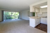 Located at 7955 Magnolia Ave in Riverside, California, this single-floor residence offers a clean, functional layout with a bright and neutral aesthetic throughout. The open-concept living and dining area is generously proportioned, featuring wall-to-wall carpet, a textured ceiling, and a sliding glass door that opens to a private balcony overlooking lush greenery — filling the space with natural light and a refreshing outdoor connection.

The kitchen is well-appointed with white cabinetry extending to the ceiling for ample storage, light-toned countertops, a gas range, built-in microwave, and a double sink. Rich hardwood-style flooring grounds the kitchen area, offering a warm contrast to the bright white finishes. A peninsula with a breakfast bar serves as a natural divider between the kitchen and living space, enhancing the open flow. A secondary wet bar or utility alcove with cabinetry is also present adjacent to the living area.

The bedroom is a comfortable, carpeted retreat with a window framing views of the surrounding trees. The bathroom features an extended vanity with generous counter space, white cabinetry below, a large wall mirror with overhead lighting, and a separate water closet. The overall ambiance is clean, airy, and move-in ready, with a consistent white and neutral palette throughout.