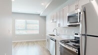 This single-floor unit presents a cohesive, modern aesthetic defined by a neutral gray color palette, wood-look plank flooring, and recessed lighting throughout. The entry hallway introduces the space with a clean, organized layout, featuring a wall-mounted panel and smart thermostat, leading naturally toward the main living and kitchen areas.

The kitchen is efficiently designed with light gray shaker-style cabinetry, stainless steel appliances including a range, dishwasher, and refrigerator, complemented by a stainless steel sink and light-toned countertops. A large window positioned above the kitchen area allows natural light to fill the space, creating a bright and functional work environment.

The bedroom areas feature the same wood-look flooring and soft gray walls, offering versatile, open spaces. One bedroom provides notable storage with two side-by-side bifold closets, each equipped with wire shelving and hanging rods. Additional rooms mirror this clean, minimalist style with multiple outlets and recessed lighting.

The bathroom maintains the unit's consistent design language with warm wood-look flooring, a full soaking tub with shower, white tile surround, and a gray vanity with ample cabinet storage. Overall, the unit delivers a modern, move-in-ready environment with practical finishes and a well-organized layout.