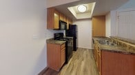 This single-floor residence is designed with an open, airy layout that maximizes comfort and functionality. The main living area is immediately impressive, boasting dramatically high vaulted ceilings that lend a sense of spaciousness and grandeur. A classic fireplace with a white mantle serves as a focal point, complemented by durable wood-look plank flooring that extends throughout the common areas.

The kitchen is efficiently laid out and features warm honey-toned cabinetry, dark granite-style countertops, black appliances including a range, microwave, and refrigerator, and a skylight that fills the space with natural light. A breakfast bar with a wraparound counter connects the kitchen seamlessly to the living and dining areas, making it ideal for both everyday living and entertaining.

The bedrooms are carpeted for comfort and each features a window with vertical blinds, allowing for natural light and privacy. Closet space is included, providing practical storage. The bathrooms are clean and functional, each equipped with a full tub-shower combination finished in crisp white surrounds with chrome fixtures.

A ceiling fan in the living area aids in climate control, and the neutral color palette throughout creates a bright, welcoming ambiance well-suited for a variety of interior styles.
