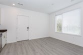 This single-floor unit presents a clean, modern aesthetic defined by a neutral color palette, light hardwood-style flooring throughout, and crisp white walls. The open-concept layout allows the kitchen and living areas to flow seamlessly together, creating a spacious and functional environment.

The kitchen is well-appointed with white shaker-style cabinetry reaching toward the ceiling, offering ample storage alongside open display shelving. Dark countertops provide a striking contrast to the light cabinetry, and the suite of stainless steel appliances — including a refrigerator, electric range, built-in microwave, and dishwasher — adds a polished, contemporary feel. A single-basin stainless steel sink with a modern faucet completes the setup.

The living area benefits from natural light streaming through window blinds, maintaining privacy while brightening the space. The entryway features a keypad-secured front door alongside an additional window, enhancing both security and light. Bedroom areas are calm and understated, with neutral taupe walls and continued hardwood-style flooring.

The bathroom is finished in an all-white scheme, featuring a vanity with white cabinetry, a toilet, and a tub-shower combination with a curved rod. Recessed lighting throughout the unit contributes to an overall bright and welcoming atmosphere.