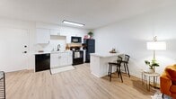 Located at 700 Morreene Rd in Durham, North Carolina, this single-floor residence offers a well-designed layout with a clean, contemporary aesthetic throughout. The kitchen serves as a functional centerpiece, outfitted with crisp white cabinetry, a deep sink, black appliances including a dishwasher, range, microwave, and refrigerator, and light wood-style flooring that extends into the main living areas. A marble-topped kitchen island with bar seating provides a convenient space for casual dining or meal prep, adding a modern touch to the open layout. The kitchen connects seamlessly to the main living area, creating an open, airy feel enhanced by bright white walls and flush lighting. The bedroom is carpeted for comfort and features neutral white walls that lend a calm, versatile atmosphere. A window allows natural light to filter into the space, making it feel welcoming and functional. The room comfortably accommodates a full-size bed and a dedicated workspace, offering flexibility for both rest and productivity. The bathroom is accessed through a private hallway and features wood-style flooring, a white vanity, a toilet, and a shower with a curtain rod. Clean finishes and a simple layout contribute to its functional, well-maintained character. Overall, the space presents a modern, move-in-ready environment suited for everyday living.
