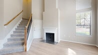 This two-story home in Lewisville, TX offers five bedrooms and four bathrooms across two floors, with the majority of the living space situated on the upper level. The main living area immediately impresses with soaring double-height ceilings, light wood-look flooring, and a wall of large windows that flood the space with natural light and provide views of the surrounding neighborhood. A classically styled white fireplace with a dark tile hearth serves as a striking focal point in the living room. A carpeted staircase with a wood banister and wrought iron balusters connects the two floors with understated elegance. The kitchen features white cabinetry, a white countertop island with a built-in sink, a tile backsplash, and stainless steel appliances, offering both functionality and a clean aesthetic. The five bedrooms are well-proportioned, with the primary bedroom providing a comfortable retreat. Bedrooms include closets with built-in shelving, and the bathrooms are finished with tub-shower combinations and light wood-look flooring. A dedicated water closet is also present. Neutral warm-beige tones throughout create a cohesive and inviting atmosphere, while ceiling fans add comfort to key living areas.