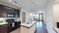 Located at 500 Coit Rd in Plano, TX, this well-appointed one-bedroom, one-bathroom unit offers a thoughtfully designed single-floor layout. The open-concept kitchen and living area serves as the heart of the unit, featuring a central island with granite countertops, an undermount sink, and elegant pendant lighting overhead. Dark espresso cabinetry, a tile backsplash, and black appliances give the kitchen a sleek, modern aesthetic. Track lighting complements the space alongside a ceiling fan in the living area, which is finished with warm hardwood-style flooring and receives natural light through a glass door offering outdoor views. The bedroom is a comfortable, carpeted retreat with a large window framing outdoor greenery and ample natural light. It connects directly to a walk-in closet outfitted with built-in shelving and hanging rods, providing generous storage. The bathroom features tile flooring and a clean, functional layout, with direct access to both the closet and hallway. A dedicated in-unit laundry area accommodates a full-size side-by-side washer and dryer with overhead shelving. Clean white walls, neutral tones, and consistent finishes throughout create a cohesive and inviting ambiance.