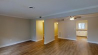 Located at 600 S Churton St in Hillsborough, NC, this two-story property offers a well-organized layout designed for comfortable everyday living. The main living area is defined by rich hardwood-style flooring that runs throughout, complemented by neutral gray walls and crisp white baseboards that create a clean, cohesive aesthetic. A ceiling fan with integrated lighting provides both comfort and illumination, while multiple doorways connect the open living space to adjacent rooms, allowing for a natural flow throughout the home. Visible HVAC vents integrated into the walls and floors reflect a thoughtfully designed climate control system. The space benefits from warm ambient lighting in the adjoining rooms, which feature the same consistent flooring and color palette, lending a sense of unity across the interior. The open passage between rooms enhances the sense of spaciousness, making the layout feel connected and accessible. With its understated finishes, functional design, and multi-level configuration, this Hillsborough property offers a straightforward and versatile living environment suited to a variety of needs.