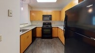 This single-floor residence in Worcester, Massachusetts offers a thoughtfully laid-out living space with a clean, neutral aesthetic throughout. The kitchen is a functional highlight, featuring warm honey-toned cabinetry with ample upper and lower storage, speckled granite-style countertops, and a full suite of black appliances including an electric range, built-in microwave, dishwasher, and refrigerator. A large skylight overhead fills the kitchen with natural light, while durable wood-look flooring adds a polished finish.

The living area is generously proportioned, with plush wall-to-wall carpeting and a notable curved bay window arrangement that draws in abundant natural light and offers views of surrounding greenery. A door provides additional access, enhancing connectivity within the layout.

The bedrooms are carpeted and bathed in natural light through large windows overlooking lush outdoor scenery, providing a calm and comfortable atmosphere. Each room offers ample wall space suitable for varied furniture arrangements.

The bathrooms are finished with light tile flooring, white vanities with under-sink storage, mirrored medicine cabinets, and multi-bulb vanity lighting. Both bathrooms include a full tub and shower combination, maintaining a clean and practical design throughout.