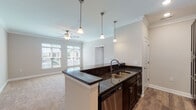 Located at 230 Club Dr in Ruckersville, Virginia, this single-floor residence offers a thoughtfully designed open-concept layout that seamlessly connects the kitchen and living areas. The kitchen is a standout feature, equipped with rich dark espresso cabinetry, dark granite countertops, a stainless steel sink with modern faucet, a stainless steel dishwasher, electric range, and over-the-range microwave. A peninsula with pendant lighting overhead serves as a natural divider between the kitchen and the living space, which is finished with warm neutral carpet, crown molding, and a ceiling fan with light fixture. Multiple windows dressed with horizontal blinds fill the living area with natural light and offer outdoor views. The bedrooms continue the warm, neutral palette with plush carpeting, ceiling fans, and ample natural light from well-placed windows. The bathroom features a dark vanity with granite countertop, a large framed mirror, stylish light bar, tile flooring, and generous storage cabinetry. Throughout the residence, consistent crown molding, neutral wall tones, and quality finishes contribute to a cohesive and comfortable living environment.