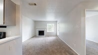This single-floor, 2-bedroom, 1-bathroom residence offers a practical and well-organized layout across a modest footprint. The living room serves as the central gathering space, highlighted by a classic fireplace with a white surround and mantel, a window and adjacent exterior door that bring in natural light and outdoor views, and neutral-toned carpet that extends throughout the main living areas. A hallway connects the living room to the rest of the unit.

The galley-style kitchen features gray cabinetry on both sides, light countertops with a double-basin sink, wood-look flooring, and black appliances including a refrigerator, electric range, and over-range microwave, making efficient use of the available space.

The primary bedroom is a generously proportioned room with carpet flooring, a walk-in closet, and an additional door providing convenient access to the hallway. The second bedroom offers carpet flooring, a window with natural light, and closet access. Both bedrooms feature textured ceilings consistent throughout the unit.

The bathroom includes wood-look tile flooring and a full tub-shower combination with white tile surround. Overall, the unit presents a clean, neutral palette well-suited for comfortable everyday living.