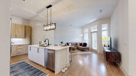 Located at Sawnee Village in Cumming, GA, this well-appointed one-bedroom, one-bathroom residence offers a thoughtfully designed open-concept layout with light wood-tone flooring flowing throughout the main living areas. The kitchen is a standout feature, showcasing natural wood-finish cabinetry, white quartz countertops, a hexagonal tile backsplash, stainless steel appliances, and a spacious island with bar seating beneath a striking industrial-style pendant light fixture — ideal for both cooking and casual dining. The kitchen opens seamlessly into the living area, which is bright and airy thanks to large windows and a glass-paneled door that invite generous natural light. The bedroom is a calm, carpeted retreat featuring a ceiling fan, a wide window with outdoor views, direct access to a dedicated walk-in closet, and a connecting hallway to the bathroom. The bathroom offers a clean, neutral aesthetic with large-format tile flooring, a gray vanity with white countertop, and a full soaking tub with shower. A dedicated in-unit laundry area with a full-size washer rounds out the practical amenities. The overall ambiance is modern, clean, and comfortable throughout.