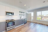 This thoughtfully designed 2-bedroom, 2-bathroom unit offers a clean, modern aesthetic across a well-utilized single floor. Light-toned wide-plank hardwood flooring flows consistently throughout, anchoring the bright, contemporary feel of the space. The open-concept kitchen and living area serves as the heart of the unit, featuring two-tone cabinetry with grey lower cabinets and white uppers, a classic white subway tile backsplash, open glass shelving, stainless steel GE appliances including a gas range, dishwasher, microwave, and French door refrigerator, and a black-accented sink fixture. Multiple large windows in the living area flood the space with natural light and offer open outdoor views. Both bedrooms are well-proportioned, each with windows providing natural light and views of the surrounding neighborhood. The primary bedroom benefits from corner windows that maximize brightness. Both bathrooms feature stone-look tile flooring, warm wood-toned vanities, matte black hardware and fixtures, and a clean, minimal design. Additional highlights include a dedicated den, in-unit laundry, six closets offering ample storage, and recessed lighting throughout. The overall ambiance is bright, modern, and move-in ready.