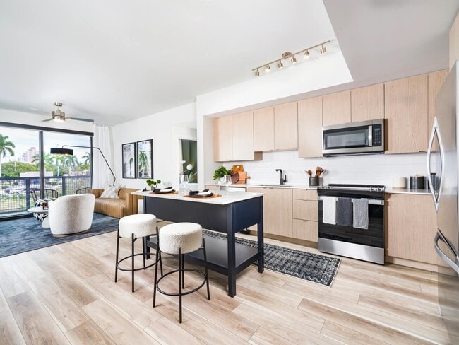 El diseño de cocina lleno de luz combina gabinetes de madera cálidos con una isla escultural, fluyendo perfectamente hacia los espacios de estar abiertos en Modera Aventura. - Modera Aventura