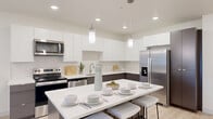 This well-designed one-bedroom, one-bathroom residence offers a thoughtfully arranged single-level floor plan with a clean, contemporary aesthetic throughout. The open-concept kitchen and living area serves as the heart of the home, featuring light wood-tone flooring, recessed lighting, and a seamless flow between spaces. The kitchen is outfitted with two-tone cabinetry — crisp white upper cabinets paired with warm taupe lower cabinets — along with stainless steel appliances including a French door refrigerator, electric range, and built-in microwave. A central island with a white quartz-style countertop provides additional prep space and seating for multiple bar stools, while pendant lighting adds a modern finishing touch. The adjoining living area is bright and airy, with natural light streaming in through a full-height sliding glass door fitted with vertical blinds, offering access to a green outdoor view. The bedroom is a comfortable retreat with carpeted flooring, a window with outdoor views, and direct access to a spacious walk-in closet featuring wrap-around hanging rods. The full bathroom includes a soaking tub and shower combo, a dark-toned vanity with a white countertop, and light wood-style flooring, maintaining the modern palette found throughout the residence.