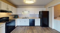 Located at 734 MacMillan Avenue in Wilmington, North Carolina, this single-floor home offers a practical and comfortable layout with a clean, neutral aesthetic throughout. The open-concept kitchen and living area serves as the heart of the home, featuring durable wood-look flooring, warm beige walls, and a textured ceiling. The kitchen is well-equipped with white shaker-style cabinetry, light countertops, a double sink, and a full suite of black appliances including a gas range, dishwasher, and refrigerator. A dedicated in-unit laundry area is conveniently accessible directly from the kitchen. The bedrooms are carpeted and finished with the same warm beige tones, providing a cozy atmosphere. One bedroom benefits from dual windows fitted with blinds, allowing for ample natural light and outdoor views. The bathroom is outfitted with wood-look flooring and features a full tub-shower combination with chrome fixtures. Throughout the home, white trim and baseboards provide a clean contrast to the warm wall tones, contributing to a cohesive and inviting interior. The single-floor layout ensures ease of navigation and a seamless flow between living spaces.
