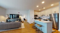 This single-floor residence offers a thoughtfully designed open-concept layout that seamlessly connects the kitchen, dining, and living areas. Warm wood-look flooring extends throughout the main living spaces, creating a cohesive and inviting atmosphere. Recessed lighting illuminates the open floor plan, complementing the clean white walls and contemporary finishes.

The kitchen is well-appointed with white shaker-style cabinetry, a classic subway tile backsplash, white quartz countertops, and a full suite of stainless steel appliances, including a gas range, microwave, refrigerator, and dishwasher. A peninsula with a light blue base and two wooden bar stools provides casual seating and additional prep space.

The living room features French doors that invite natural light and offer outdoor access. A dining area sits adjacent, rounding out the open main living space.

The primary bedroom offers a serene retreat with neutral tones, hardwood-style flooring, and ample natural light through shuttered windows. A second bedroom features a striking starry night accent wall mural, adding a distinctive character to the space.

The bathroom includes hexagonal tile flooring, a tub-shower combination with chevron-patterned tile surround, and clean white fixtures, completing the home's modern aesthetic.