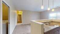 This single-floor residential unit offers a thoughtfully designed layout that balances functionality and comfort. The open-concept kitchen serves as a central highlight, featuring dark wood cabinetry, granite-style countertops, a double-basin sink, and a full suite of stainless steel appliances including a refrigerator, electric range, and built-in microwave. Light wood-style flooring runs throughout the kitchen, and pendant lighting above the peninsula adds a modern touch. The peninsula itself creates a natural transition into the carpeted living area, which flows toward a connecting hallway accented with warm yellow walls, providing a welcoming passage to the rest of the unit. Two generously sized bedrooms are finished with plush carpeting and feature windows fitted with horizontal blinds, allowing natural light to filter in while maintaining privacy. The unit includes two bathrooms: one equipped with a full soaking tub and shower combination, and a second featuring a standalone walk-in shower stall, both finished with light wood-style flooring and neutral wall tones. The overall color palette of soft beige and cream throughout creates a clean, understated ambiance that is both versatile and move-in ready.