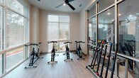 Located at 2245 Interstate North Pkwy SE in Atlanta, Georgia, this single-floor fitness studio is a well-appointed exercise space designed to support a wide range of workout routines. The room is bright and airy, thanks to expansive floor-to-ceiling windows fitted with adjustable blinds that frame views of surrounding greenery and the outdoor landscape. A ceiling fan overhead helps maintain comfortable airflow throughout workout sessions.

The studio is equipped with multiple stationary cycling bikes arranged to take full advantage of the natural light, creating an energizing environment for indoor cycling. Along the walls and on mobile racks, an assortment of color-coded dumbbells offers a complete range of free weight options, while a dedicated rack holds stability and exercise balls in various sizes. Step platforms and soft plyo boxes are neatly stacked in the corner, providing tools for aerobic and plyometric training.

Glass-panel walls on one side offer a visual connection to an adjacent fitness area, adding a sense of openness and depth. The light wood-toned flooring throughout gives the space a clean, modern aesthetic. Thoughtfully organized and comprehensively equipped, this fitness studio delivers a professional-grade workout environment suited for cardio, strength, and functional training alike.