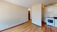 Located on Colfax Ave S in the vibrant Kingfield neighborhood of Minneapolis, this single-floor unit offers a straightforward and functional layout. The main living area is finished with warm wood-style laminate flooring and neutral-toned walls, creating a bright and open feel. A peninsula with a dark countertop partially separates the kitchen from the living space, providing a natural division while maintaining an open flow. Windows along the living area allow natural light to filter in, and baseboard heating runs along the perimeter of the room.

The kitchen is compact and efficiently arranged, featuring white cabinetry extending to the ceiling, a gas range, dark granite-style countertops, and a full-size refrigerator. Storage is maximized with upper cabinets stacked overhead.

The bedroom is carpeted and includes a ceiling fan, a window with an outdoor view, and baseboard heating. The hallway connecting the rooms features rich wood-toned doors that add a warm contrast to the lighter walls and flooring throughout.

The bathroom retains a classic retro character, with pink tile wainscoting, a wall-mounted sink, and coordinating floor tile, all framed by a mirrored medicine cabinet and a rich wood door.