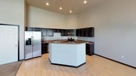 This two-floor home offers a functional and well-designed layout with notable architectural details throughout. The main living area is highlighted by soaring vaulted ceilings and large black-framed windows that invite generous natural light, creating an open and airy atmosphere. A fireplace anchors the carpeted living room, adding a warm focal point to the space. Adjacent to the living area, the open-concept kitchen is well-equipped with dark espresso cabinetry extending to ceiling height, granite countertops, a central island, and a full suite of stainless steel appliances including a refrigerator, range, built-in microwave, and dishwasher. Light hardwood-style flooring runs throughout the kitchen and dining area.

The bedrooms are carpeted and neutrally finished, offering comfortable and versatile living spaces. The upper level includes a carpeted bedroom with soft neutral walls, while the lower level provides an additional bedroom with a small window and flush-mount lighting. Multiple bathrooms are present, each featuring white walk-in showers or a shower-tub combo and granite-accented vanities. The lower level also houses a dedicated laundry room with a washer and dryer, exposed concrete walls, and utility connections.