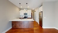 Located at 2817 Girard Ave S in the vibrant Uptown neighborhood of Minneapolis, this single-floor residence offers a thoughtfully designed layout with contemporary finishes throughout. The open-concept kitchen serves as the centerpiece of the living space, featuring rich dark wood cabinetry contrasted by crisp white upper cabinets and quartz countertops. A central island with an integrated stainless steel sink and elegant pendant lighting provides both functionality and visual appeal. Stainless steel appliances — including a gas range, microwave, and refrigerator — are complemented by a classic geometric tile backsplash. A sliding barn door adds a stylish architectural touch near the entryway. Rich hardwood floors flow seamlessly through the kitchen and living areas, where natural light streams in through a large sliding glass door fitted with vertical blinds. Ceiling fans in both the living area and bedroom contribute to a comfortable atmosphere year-round. The bedroom offers plush carpeting and a spacious walk-in closet with wire shelving and built-in organizers. The bathroom is finished with a dark wood vanity, white quartz countertop, and a large mirror with overhead lighting, maintaining the cohesive modern aesthetic found throughout the entire space.
