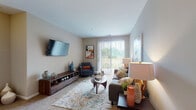 Located at 1375 S White Oak Dr in Waukegan, Illinois, this single-floor residence offers a thoughtfully designed layout that balances comfort and functionality. The living room serves as the heart of the home, featuring neutral-toned walls, plush carpeting, and a large sliding glass door with vertical blinds that floods the space with natural light and provides direct access to an outdoor area with open green views. A wall-mounted flat-screen television and a sleek low-profile media console anchor the room, complemented by a cohesive arrangement of seating and décor. The kitchen is designed for practicality, featuring light wood cabinetry extending to the ceiling, a breakfast bar peninsula, track lighting, and a full suite of appliances including a range and dishwasher. An adjacent dining nook provides a dedicated space for meals. The residence includes multiple bedrooms, each finished with soft carpeting, generous natural light from large windows dressed with sheer curtains, and ample room for full bedroom furniture sets. The bathroom is equipped with a tub-shower combination, a vanity with storage, and tile flooring. Throughout the home, a cohesive warm and neutral color palette creates a calm, inviting ambiance suited to everyday living.
