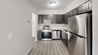 Located at 310 Shipley Rd in Wilmington, Delaware, this one-bedroom, one-bathroom residence offers a well-organized single-floor layout designed for comfortable living. The living room is a standout space, featuring plush wall-to-wall carpeting, neutral gray tones, and a large sliding glass door dressed with vertical blinds that floods the room with natural light and provides outdoor access. The layout flows naturally into the kitchen, which is outfitted with dark espresso-toned shaker-style cabinetry, light stone-finish countertops, and a full suite of stainless steel appliances including a range, dishwasher, and refrigerator. Light-toned luxury vinyl plank flooring completes the kitchen's modern aesthetic. The generously sized bedroom offers a comfortable retreat with soft carpeting, a window with blinds that allows ample natural light, and a double-door closet providing substantial storage. The bathroom features a tub and shower combination with clean white subway tile surround and a glass enclosure, lending a fresh, updated feel. Throughout the residence, neutral wall colors, clean white trim, and consistent finishes create a cohesive and move-in-ready atmosphere.