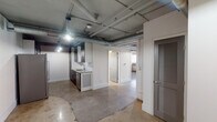 Located at 1907 Second Ave N in downtown Birmingham, Alabama, this single-floor loft-style unit offers a distinctly industrial aesthetic rooted in its historic building origins. Exposed metal ductwork runs across the ceilings throughout, complemented by polished and raw concrete floors that reinforce the urban character of the space.

The galley-style kitchen is well-appointed with dark cabinetry, granite countertops, a subway tile backsplash, stainless steel appliances including a French door refrigerator, gas range, and dishwasher, and pendant lighting overhead. An open layout connects the kitchen to the main living area, which benefits from ceiling-mounted industrial barn lights.

The bedroom features dual sets of arched gray double doors providing generous closet storage, a ceiling fan, and a window that brings in natural light, with sections of the original brick wall exposed beneath peeling plaster — a raw, authentic nod to the building's history.

The bathrooms offer contrasting finishes: one includes a soaking tub and walk-in shower enclosed by a glass panel, with marble-style tile surround and penny tile flooring, while the second features a tub-shower combo with travertine tile walls. The open ceiling structure with visible piping and ductwork throughout unifies the space with a consistent industrial loft sensibility.