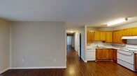 This single-story residence in South Carolina offers a practical and cohesive layout highlighted by rich, dark hardwood-style flooring that runs consistently throughout the home. The open living area is bright and welcoming, featuring a large sliding glass door fitted with vertical blinds that invite natural light and provide access to the outdoors. Neutral-toned walls complement the flooring and create a clean, versatile backdrop throughout the space.

The kitchen is well-appointed with warm honey-toned wood cabinetry extending to the upper walls for generous storage, white appliances including a range, dishwasher, and refrigerator, and a double-basin sink set into light countertops. A textured ceiling and overhead fluorescent lighting round out the functional design.

A hallway connects the main living area to the private quarters, which include several bedrooms. Each bedroom features the same dark hardwood-style flooring, neutral walls, and white six-panel doors, with some rooms benefiting from windows that bring in additional natural light. The bathroom includes a full tub and shower combination with clean white surround and chrome fixtures, with an additional bathroom also featuring a soaking tub. White trim and baseboards tie each room together, giving the entire home a consistent and tidy aesthetic.