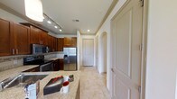 This thoughtfully designed 1-bedroom, 1-bathroom floor plan offers a comfortable and functional living environment across a single level. The kitchen serves as a central highlight, showcasing warm wood cabinetry, granite countertops with subtle veining, and a full suite of stainless steel appliances including a French door refrigerator, microwave, and range. Track lighting overhead ensures the kitchen is well-lit and practical. Light-toned tile flooring flows throughout the space, lending a clean and cohesive aesthetic. Elegant crown molding frames the ceilings, adding a refined architectural touch to the interior. A graceful arched doorway provides a decorative transition between spaces, contributing to the unit's classic character. The hallway connects the living areas to the private bedroom and bathroom, maintaining an efficient and intuitive layout. Recessed lighting complements the overall brightness of the space. The combination of quality finishes, classic detailing, and a practical floor plan makes this residence a well-rounded living space suited for everyday comfort.
