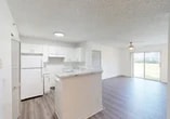 This single-story, 4-bedroom, 2-bathroom home in Fort Myers, Florida offers a practical and well-appointed layout designed for comfortable living. The open-concept kitchen and living room form the heart of the home, where a peninsula with marble-look countertops serves as a natural dividing point. The kitchen is outfitted with crisp white cabinetry, ample storage, and a full-size refrigerator, while wood-look plank flooring extends seamlessly into the living area. A ceiling fan overhead and a sliding glass door at the far end of the living room bring in natural light and outdoor views, adding an airy feel to the space. The four bedrooms are well-sized, with the generously proportioned primary bedroom offering substantial square footage for a comfortable retreat. Bedrooms feature built-in closets with wire shelving for organized storage, and at least one walk-in closet provides additional capacity. Both bathrooms include tub-shower combos with clean white tile surrounds. A dedicated laundry area with an in-unit washer adds everyday convenience. Textured ceilings and neutral wall tones throughout create a clean, move-in-ready aesthetic suited for a variety of furnishing styles.