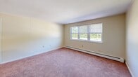 Located at 82 Jerome Rd in Uncasville, Connecticut, this single-floor unit offers three bedrooms and one bathroom within a compact, efficiently arranged layout. The bedrooms are finished with soft wall-to-wall carpeting in a warm neutral tone and feature cream-colored walls that lend a clean, understated look. Multiple windows throughout the bedrooms invite natural light and provide views of the surrounding greenery. Baseboard heating runs along the walls, ensuring consistent warmth throughout the cooler seasons. The generously sized primary bedroom includes two separate doors, one leading to a closet and the other to an adjacent room, adding a degree of privacy and flexibility. The kitchen features wood-toned cabinetry, a countertop with a built-in sink, and tile flooring, providing a practical workspace at the heart of the home. The single full bathroom is appointed with pink accent wall tiles, a tub-shower combination, a wood-toned vanity with a white countertop, and stone-look tile flooring, giving the space a retro character. The overall layout, as seen in the floor plan view, positions the kitchen centrally between the living and bedroom areas, offering a straightforward and functional flow throughout the home.