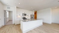 This well-appointed 2-bedroom, 2-bathroom residence offers a thoughtfully designed single-level layout filled with natural light and contemporary finishes throughout. The open-concept kitchen and living area serves as the heart of the home, anchored by a generously sized island topped with striking granite countertops. White shaker cabinetry, a classic subway tile backsplash, and a full suite of stainless steel appliances — including a range, microwave, and French door refrigerator — complete the kitchen. Light wood-tone flooring extends throughout the main living areas, lending a clean, cohesive aesthetic. The living room benefits from large windows and sliding glass doors that open to a private balcony, offering open outdoor views and abundant natural light. A ceiling fan adds comfort to the space. Both bedrooms feature plush carpeting and ample natural light, with the primary bedroom providing generous proportions. Three closets, including a large walk-in with built-in shelving and hanging rods, offer excellent storage. The bathrooms are finished with granite vanity tops, white cabinetry with matte black hardware, and a tiled tub-shower surround. An in-unit washer adds everyday convenience. The overall ambiance is bright, modern, and move-in ready.