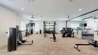 Located at 5171 Bowman Rd in Macon, Georgia, this single-story fitness facility offers a generously sized, thoughtfully designed workout space divided into two functional zones. The main strength training area features plush carpeted flooring and is bathed in natural light from multiple windows fitted with blinds. The room is equipped with a multi-station cable machine, weight bench, adjustable dumbbells on a tiered rack, a seated press machine, and a rowing bench, providing comprehensive strength training options. Dual ceiling fans keep the space comfortable during intense workouts, while a large wall-mounted mirror amplifies the sense of openness and allows for form monitoring. A secondary cardio zone features durable dark rubber flooring and houses two treadmills, a stair climber, and an elliptical machine. This area also benefits from natural light and includes a large mirror wall that visually expands the space. A classic wood-framed glass door provides direct outdoor access, enhancing convenience and ventilation. The clean, neutral white walls and bright recessed lighting throughout both areas create an inviting, professional atmosphere well-suited for a comprehensive fitness regimen.