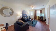 Located at Bermuda Run in Statesboro, Georgia, this single-floor unit offers a thoughtfully laid-out living space with multiple bedrooms, two bathrooms, and practical amenities throughout. The living room serves as the heart of the home, featuring rich hardwood-style flooring, a ceiling fan, and windows dressed with curtains that allow natural light to fill the space. An open sightline connects the living area to the dining space and kitchen, creating a cohesive and functional common area. The kitchen is outfitted with black appliances, including a range, over-the-range microwave, and refrigerator, complemented by white cabinetry and tile flooring. The bedrooms feature hardwood-style floors, ceiling fans, and windows with blinds that provide natural light and privacy. Each room offers space for a bed and desk, making them well-suited for both rest and study. The two bathrooms include tile flooring and warm wood-toned vanity cabinetry; one features a shower-tub combination, while the other includes a shower with a decorative curtain. A dedicated in-unit laundry area houses a full-size washer and dryer with overhead shelving for added storage. Throughout the unit, neutral wall tones and consistent flooring materials create a cohesive and inviting atmosphere.