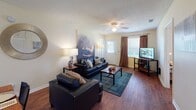 Located at Bermuda Run in Statesboro, Georgia, this single-floor unit offers a thoughtfully laid-out living space with multiple bedrooms, two bathrooms, and practical amenities throughout. The living room serves as the heart of the home, featuring rich hardwood-style flooring, a ceiling fan, and windows dressed with curtains that allow natural light to fill the space. An open sightline connects the living area to the dining space and kitchen, creating a cohesive and functional common area. The kitchen is outfitted with black appliances, including a range, over-the-range microwave, and refrigerator, complemented by white cabinetry and tile flooring. The bedrooms feature hardwood-style floors, ceiling fans, and windows with blinds that provide natural light and privacy. Each room offers space for a bed and desk, making them well-suited for both rest and study. The two bathrooms include tile flooring and warm wood-toned vanity cabinetry; one features a shower-tub combination, while the other includes a shower with a decorative curtain. A dedicated in-unit laundry area houses a full-size washer and dryer with overhead shelving for added storage. Throughout the unit, neutral wall tones and consistent flooring materials create a cohesive and inviting atmosphere.