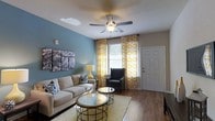 Located at 3245 Glen McConnell Parkway in Charleston, South Carolina, this single-floor residence combines comfortable living with thoughtfully designed interiors. The living area serves as the heart of the home, showcasing rich hardwood-style flooring that runs throughout and adds warmth to the space. A soothing teal accent wall provides a pop of color, complemented by crisp white trim and ceilings. A ceiling fan keeps the room comfortable year-round, while large windows dressed in vibrant yellow patterned curtains invite generous natural light and lend a cheerful, welcoming ambiance. The living space is well-proportioned, offering ample room for seating and entertaining. Décor-ready walls and modern furnishing arrangements highlight the versatility of the layout. The front entry features a classic paneled door, providing a clean, traditional architectural detail. Overall, this residence strikes a balance between contemporary style and everyday functionality, with light-filled rooms, cohesive color choices, and quality flooring finishes that create an inviting atmosphere throughout. Its single-level layout ensures convenient, easy living in the well-established Charleston community of Glen McConnell Parkway.