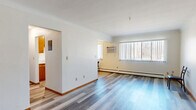 Located at 1445 Minnehaha Ave E in Saint Paul, Minnesota, this single-floor, 2-bedroom, 1-bathroom unit offers a practical and comfortable layout. The open living room is a standout feature, showcasing wide-plank laminate flooring in a cool gray tone, large windows with vertical blinds that allow ample natural light, a wall-mounted air conditioning unit, and baseboard heating — ensuring year-round comfort. A wood-framed entry door adds a classic touch to the space.

The kitchen is equipped with warm oak cabinetry, stainless steel appliances including a range and refrigerator, a ceiling fan, and tile flooring. It offers a functional galley-style layout with generous counter space and direct access to the bathroom.

The full bathroom features a tiled tub-and-shower combination, a vanity with wood cabinetry, mosaic tile flooring, and a wall mirror. Both bedrooms continue the laminate flooring theme, each offering windows with blinds and baseboard heating. The generously sized primary bedroom includes dual windows, providing additional natural light and ventilation.

A connecting hallway ties the rooms together efficiently. This well-organized unit delivers essential amenities in a straightforward, functional layout ideal for everyday living in the East Saint Paul neighborhood.