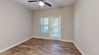 Located at 121 Village Green Ln in Mooresville, NC, this one-bedroom, one-bathroom unit offers a well-organized, single-level layout that maximizes every square foot of its compact footprint. The open-concept living, dining, and kitchen area forms the heart of the home, with wood-look hard-surface flooring running throughout the main living spaces. The kitchen is a standout, featuring rich dark-brown cabinetry, granite-style countertops, a classic white subway tile backsplash, and stainless steel appliances including a range, microwave, and refrigerator. A ceiling fan and exterior door in the living area provide both comfort and direct outdoor access, while window blinds allow for natural light control. The bedroom is finished with plush wall-to-wall carpeting and a large window that frames views of the surrounding greenery, creating a calm and restful atmosphere. The bathroom includes a full soaking tub and shower combo with tiled surround, brushed nickel fixtures, and wood-look flooring for a clean, cohesive finish. A dedicated in-unit laundry space accommodates a full-size top-loading washer and dryer with overhead wire shelving for added storage. Neutral wall tones and white trim throughout give the space a clean, move-in-ready appeal.