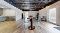 Located at 3819 Plane Tree Dr W in Columbus, Ohio, this single-floor commercial space offers a compelling blend of industrial and refined design elements across four distinct rooms. The open main area showcases a dramatic exposed black steel ceiling with warm bistro string lighting, white-painted brick walls, and durable wood-look flooring — creating a welcoming yet edgy atmosphere well-suited for a variety of uses. A dedicated lounge area mirrors this industrial character with the same exposed ceiling, painted brick walls, and hardwood-style floors, providing a comfortable and flexible gathering zone. A thoughtfully designed kitchenette stands out with its slate-tiled accent walls, soft blue cabinetry with glass-front upper doors, light quartz countertops, an under-counter beverage refrigerator, and recessed lighting — offering both style and functionality. An additional room features a cleaner, more refined finish with smooth white walls, the same exposed ceiling detail, and ample open floor space, ideal as an office, consultation area, or studio. Throughout the space, consistent flooring and cohesive design details tie each room together into a polished, multi-functional environment with strong character and broad appeal.